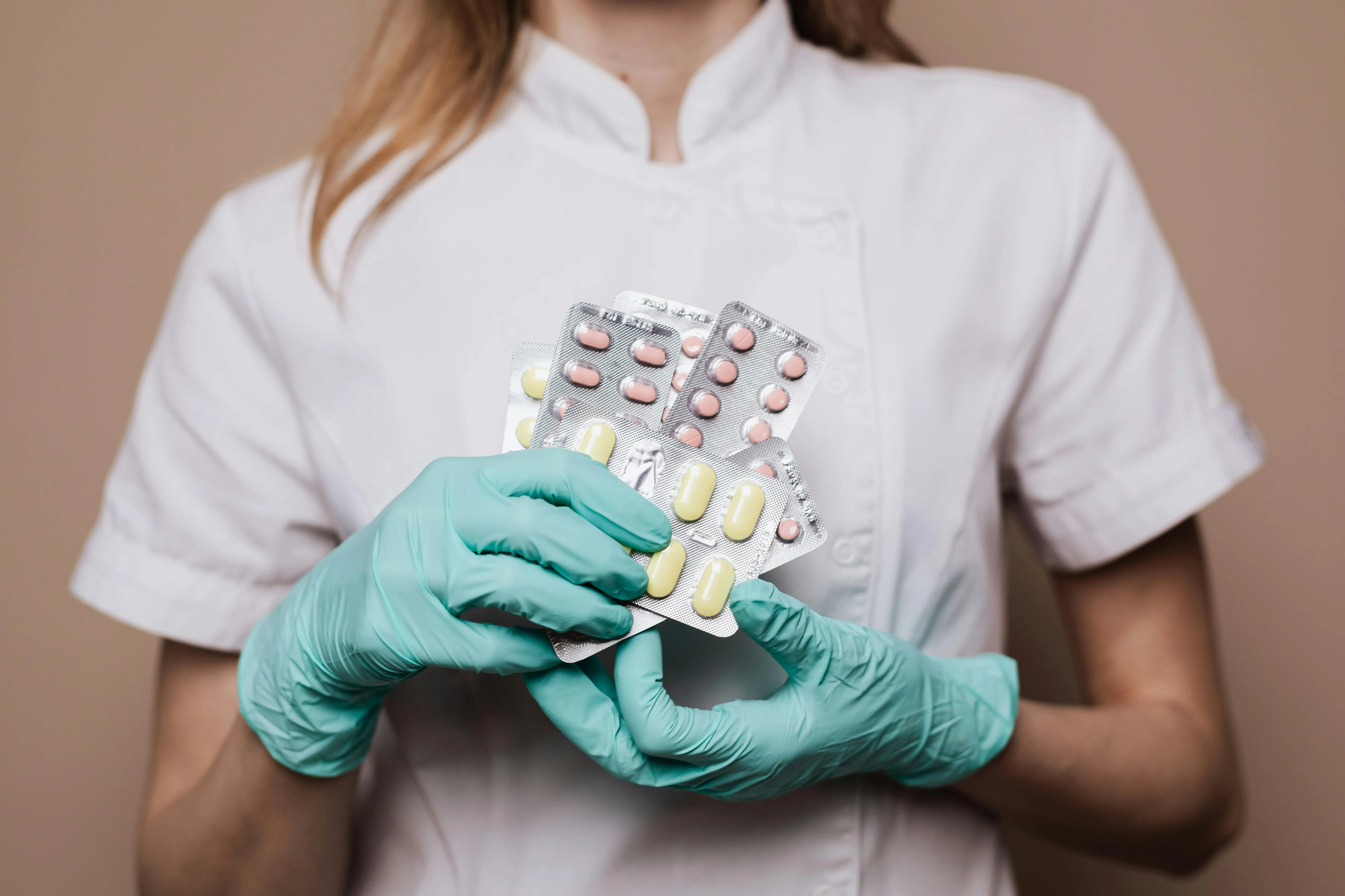 photo of female doctor with gloves on holding different packets of pills and medications